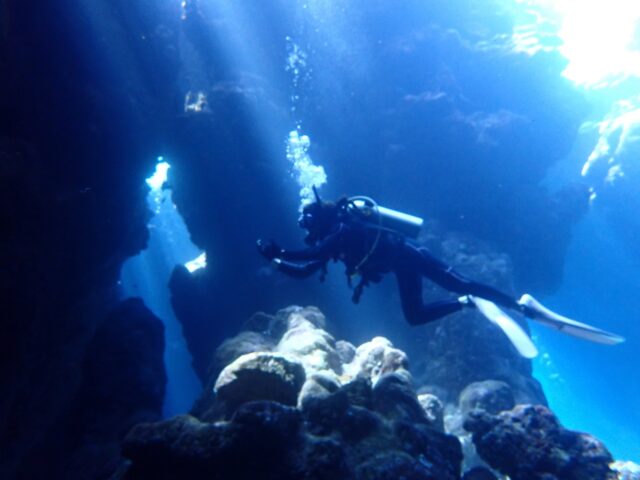 宮古島の水中洞窟に差し込む光のカーテン（光の柱）とダイバー