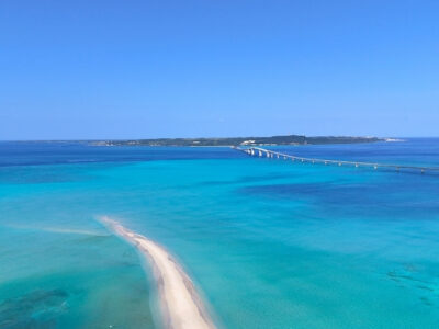 ユニの浜のドローン撮影。宮古島の青いグラデーションの海に、一筋の白い砂洲とクリアSUPが浮かぶ絶景