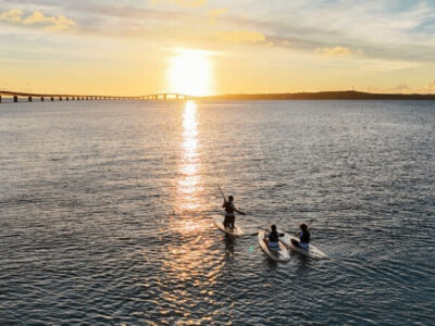 宮古島の伊良部大橋を背景に、夕暮れ時の海でSUPを楽しむ人々のシルエット