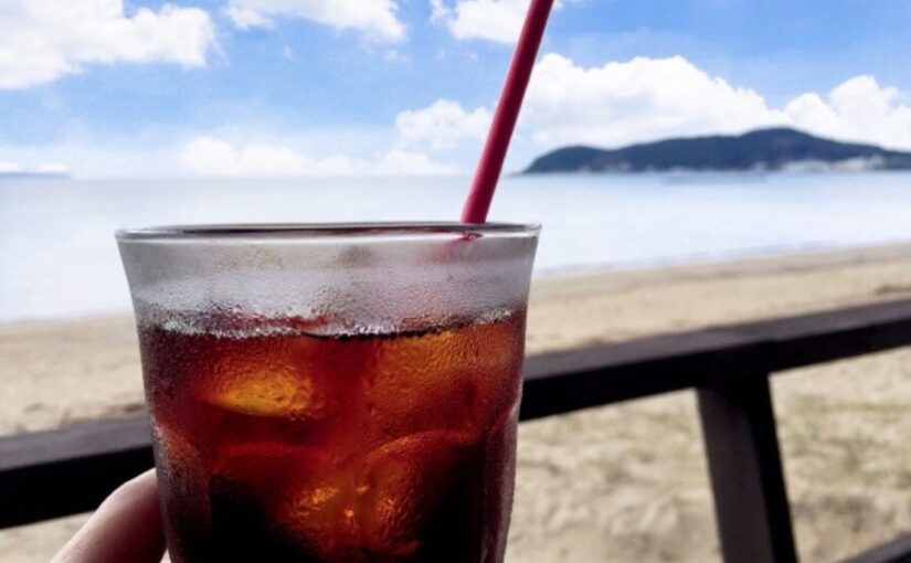 砂浜と海を背景にした赤いストローのアイスコーヒー