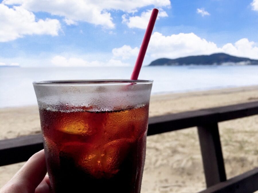 砂浜と海を背景にした赤いストローのアイスコーヒー