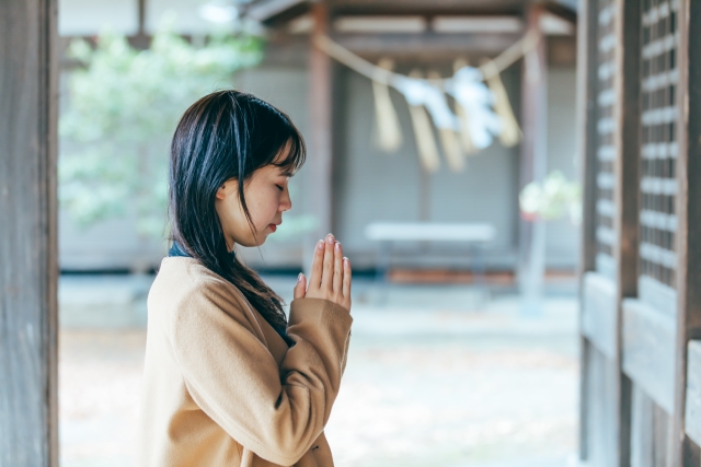 神社の拝殿前でお参りのマナーを守る女性